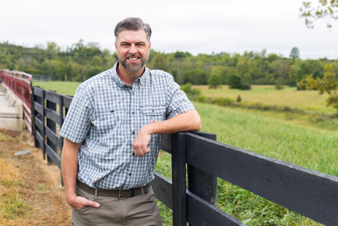 Senator Jared Carpenter leaning on a plank fence beside a Kentucky pasture